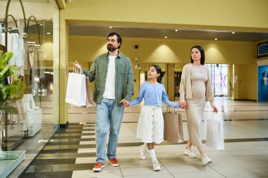 Mutlu bir aile alışveriş merkezinden geçiyor, alışveriş torbaları taşıyor ve birlikte vakit geçiriyorlar..