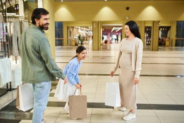 A happy man and woman stroll through a mall, carrying shopping bags filled with their latest purchases. clipart