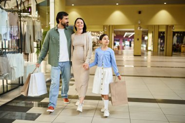 Alışveriş çantalı mutlu bir aile eğlenceli bir hafta sonu gezisinde alışveriş merkezinden geçiyor..