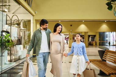Alışveriş torbaları taşıyan mutlu bir aile, kalabalık bir alışveriş merkezinde birlikte geziyor..