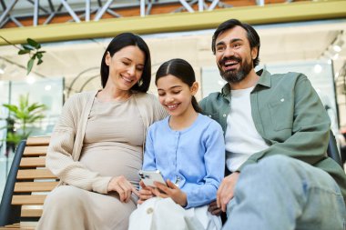 A joyful family of four sitting together on a bench in a bustling shopping mall, smiling and enjoying their time. clipart