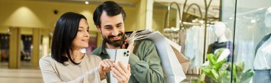 Meşgul bir alışveriş merkezinin ortasında cep telefonuna dalmış bir adam ve kadın.