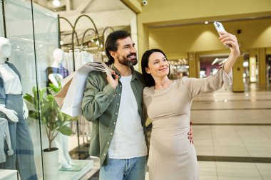 Bir erkek ve kadın alışveriş merkezinde alışveriş yaparken mutlu bir şekilde selfie çekiyorlar..