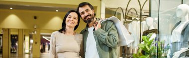 A man and woman joyfully navigate a mall, clutching shopping bags filled with their weekend finds. clipart