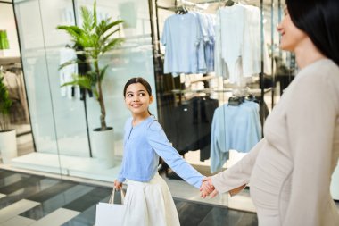 Neşeli bir anne-kız alışveriş merkezinde el ele yürürler, eğlenceli bir aile gezisinin tadını çıkarırlar..