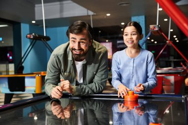 A dad and daughter engage in an intense game of air hockey at a gaming zone in a mall, having a fun family weekend. clipart