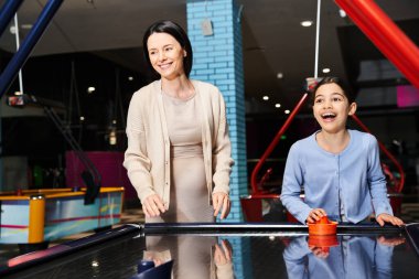 Bir anne ve kızı, çarşıda eğlenceli bir hafta sonu gezisinde atari salonunda neşeyle hokey oynuyorlar..