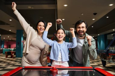 A joyful family competes in a lively game of air hockey in an arcade, surrounded by flashing lights and the sound of laughter. clipart