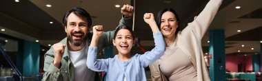 A delighted family raises their arms in a malls gaming zone, celebrating unity and happiness during a weekend outing. clipart