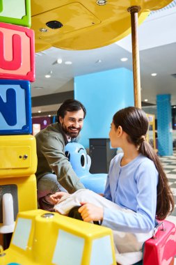 father and child happily play with a toy car in a malls gaming zone during the weekend. clipart