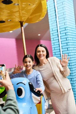 A joyful mother and child capturing a moment while riding a toy carousel in a malls gaming zone during the weekend. clipart