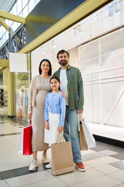 Bir alışveriş merkezinde mutlu bir aile duruyor, her biri hafta sonu eğlencesinden aldıklarıyla dolu bir sürü alışveriş çantası taşıyor..