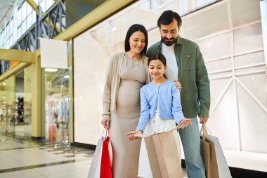 Alışveriş torbalarıyla dolu mutlu bir aile kalabalık bir alışveriş merkezinde hafta sonunun tadını çıkarıyor, birlikte özel anılar yaratıyor..