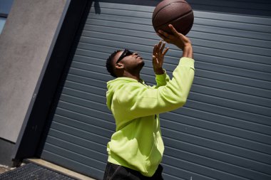 Handsome man in green hoodie catches basketball. clipart