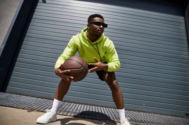 Yeşil kapüşonlu, elinde basketbol topuyla şık bir Afrikalı Amerikalı..