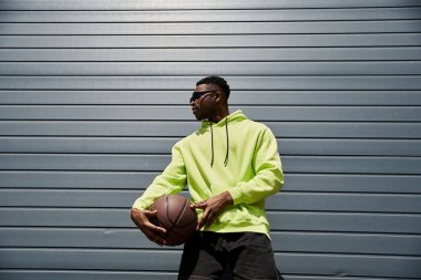 Havalı, neon kapüşonlu, elinde basketbol tutan Afrikalı Amerikalı bir adam..