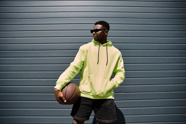 Neon kapüşonlu genç Afrikalı Amerikalı adam, elinde basketbol topu var..