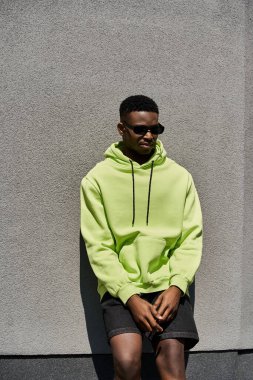 Neon yeşil kapüşonlu şık Afro-Amerikan adam duvara yaslanıyor..