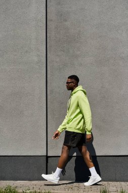 Fashionable African American male in green hoodie walking down street. clipart