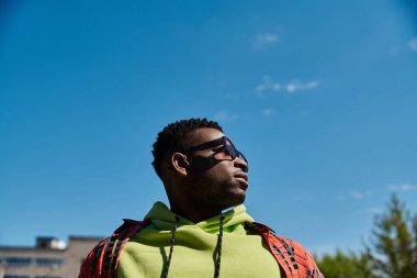 Handsome African American man in green hoodie gazes up at the sky. clipart