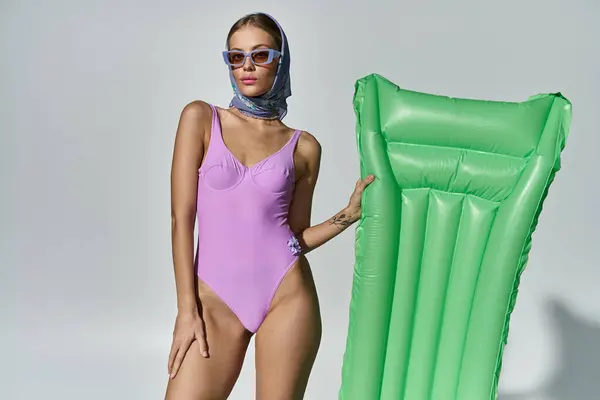 stock image Fashionable woman in a purple swimsuit strikes a pose next to a green inflatable mattress.