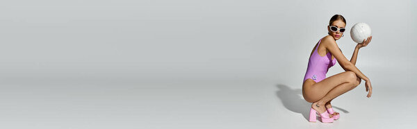 Stylish woman with blonde hair crouches gracefully in a pink swimsuit.