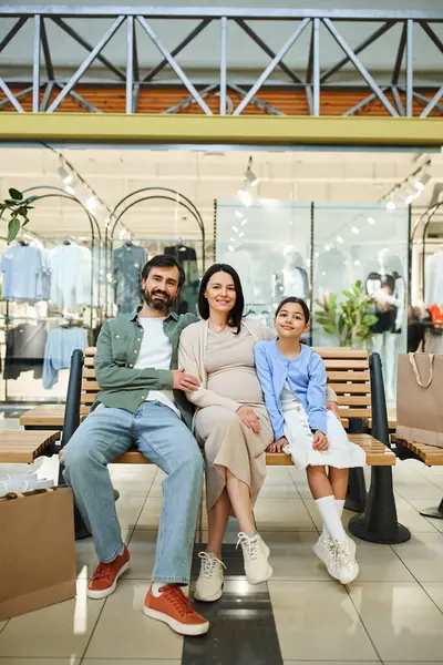 stock image A family smiling and relaxing on a bench inside a bustling shopping mall on a weekend.