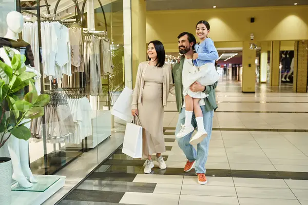 stock image A happy family, parents and kid, leisurely walk through a bustling shopping mall on a weekend outing.