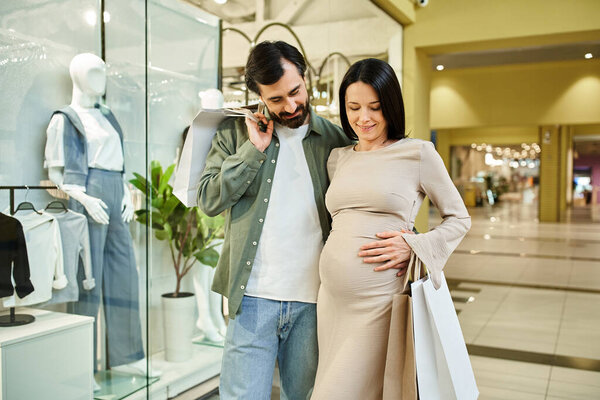 A pregnant man and woman happily walk through a bustling shopping mall on a weekend outing.