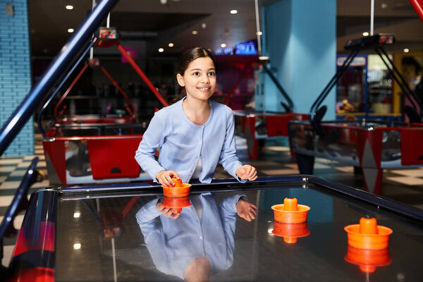 A young girl energetically playing air hockey in a mall gaming zone
