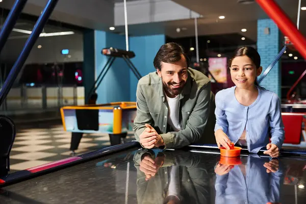 stock image A man and child engage in a thrilling match of air hockey, competing with smiles and intensity in a vibrant gaming zone.
