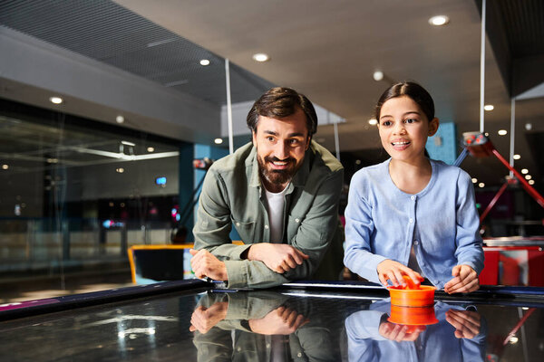 A man and kid joyfully compete in a lively game of air hockey in an arcade at a mall on the weekend.