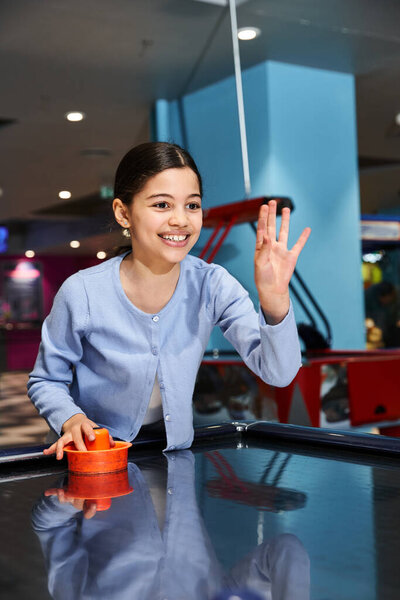 A girl joyfully competes in a game of air hockey with family at a mall gaming zone during the weekend.