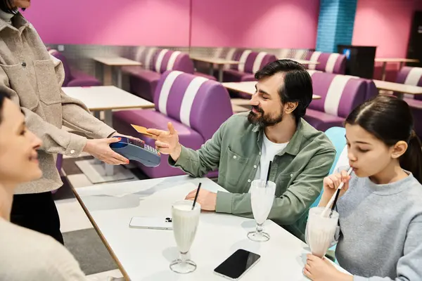stock image A happy family sits at a restaurant table, man handing a credit card to a waitress