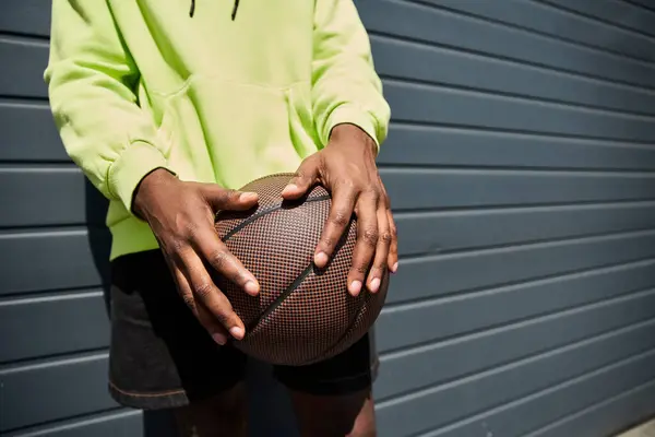 stock image African American male in fashionable attire holding basketball against wall.