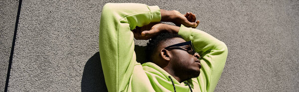 Красивый афроамериканец в зеленой толстовке прислонился к стене.