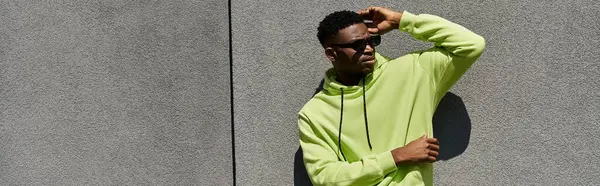 stock image Handsome African American man leaning against wall in stylish green hoodie.