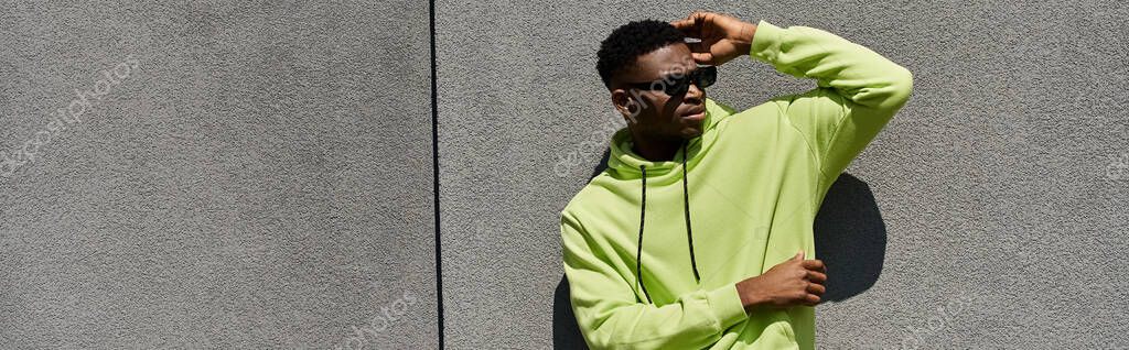 Handsome African American man leaning against wall in stylish green hoodie.