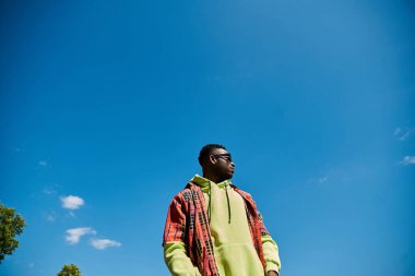 Mavi gökyüzünün altındaki bir tarlada duran şık bir Afrikalı Amerikalı..