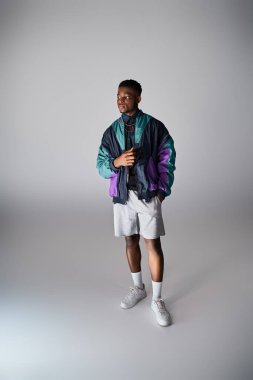 Renkli ceketli ve şortlu yakışıklı Afro-Amerikan adam beyaz bir arka plana zarif bir şekilde poz veriyor..