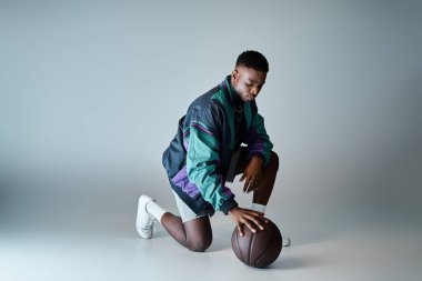 Fashionable young African American man in stylish attire crouching with basketball. clipart