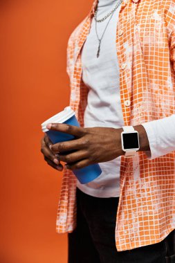 Handsome man in orange shirt savoring cup of coffee. clipart