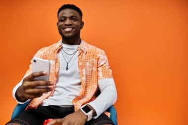 Cep telefonu kullanırken sandalyede oturan şık giyimli yakışıklı Afro-Amerikan adam..
