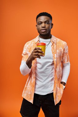 Yakışıklı Afro-Amerikalı şık giyinmiş parlak turuncu bir fonda bir fincan kahvenin tadını çıkarıyor..
