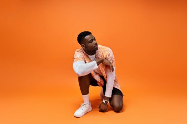 Yakışıklı Afro-Amerikalı şık giyinmiş canlı turuncu arka planda çömelmiş..