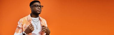 Gözlüklü yakışıklı Afro-Amerikan genç adam cesur turuncu arka planda poz veriyor..