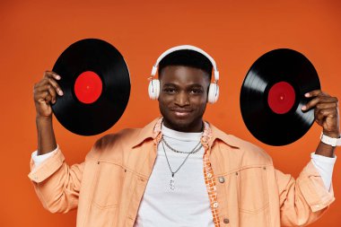 Handsome black man holding vinyl records against orange background. clipart