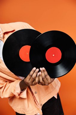 Handsome African American man holding two vinyl records against an orange background. clipart