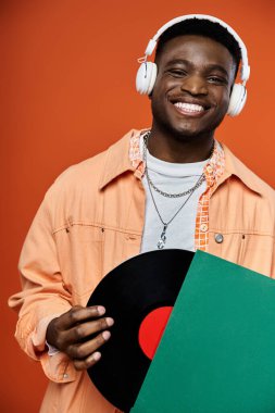 Stylish young African American man holding a record and wearing headphones. clipart