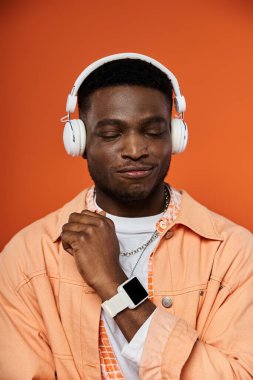 Stylish African American man in headphones against vibrant orange backdrop. clipart